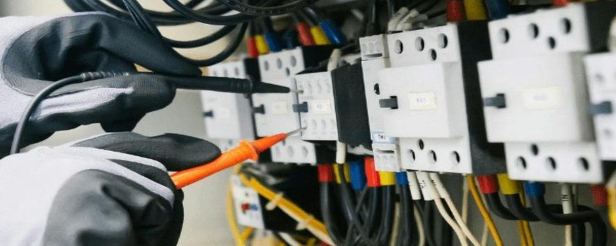 Gloved hands using test probes inside an electrical control panel
